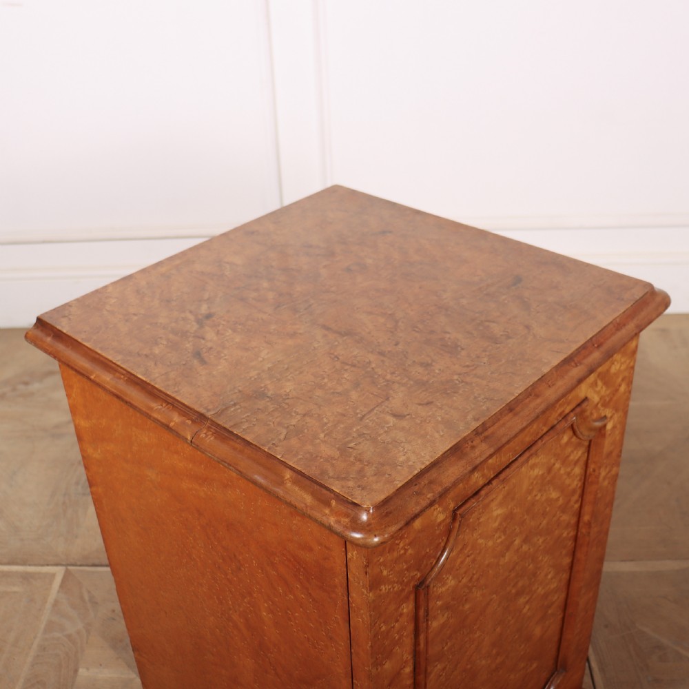 A golden brown burr elm bedside cabinet featuring a single panelled cupboard door and a solid plinth base. View VI