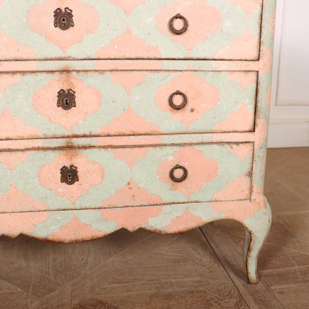 An Italian style three-drawer painted wooden commode featuring a pastel pink and green geometric pattern, brass ring pulls, and a terracotta marble top. View VI