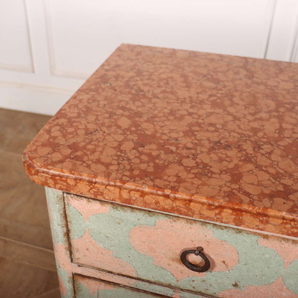 An Italian style three-drawer painted wooden commode featuring a pastel pink and green geometric pattern, brass ring pulls, and a terracotta marble top. View VII