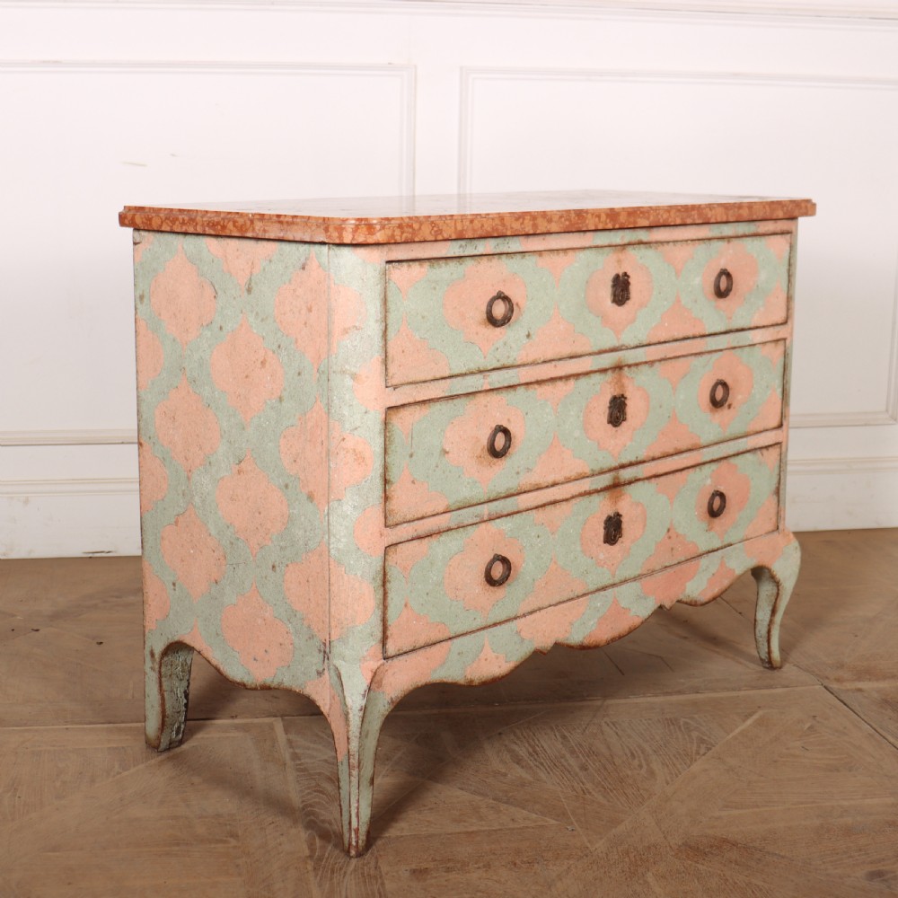 An Italian style three-drawer painted wooden commode featuring a pastel pink and green geometric pattern, brass ring pulls, and a terracotta marble top. View VIII