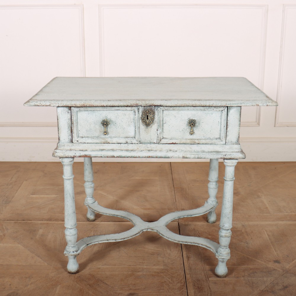 An 18th-century painted wooden side table featuring a pale blue distressed surface, turned legs, an X-frame stretcher, and two drawer fronts with brass pulls.