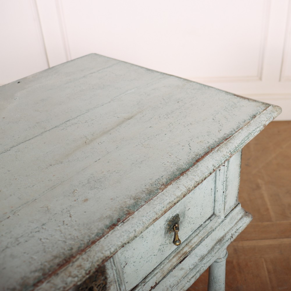 An 18th-century painted wooden side table featuring a pale blue distressed surface, turned legs, an X-frame stretcher, and two drawer fronts with brass pulls. View VII