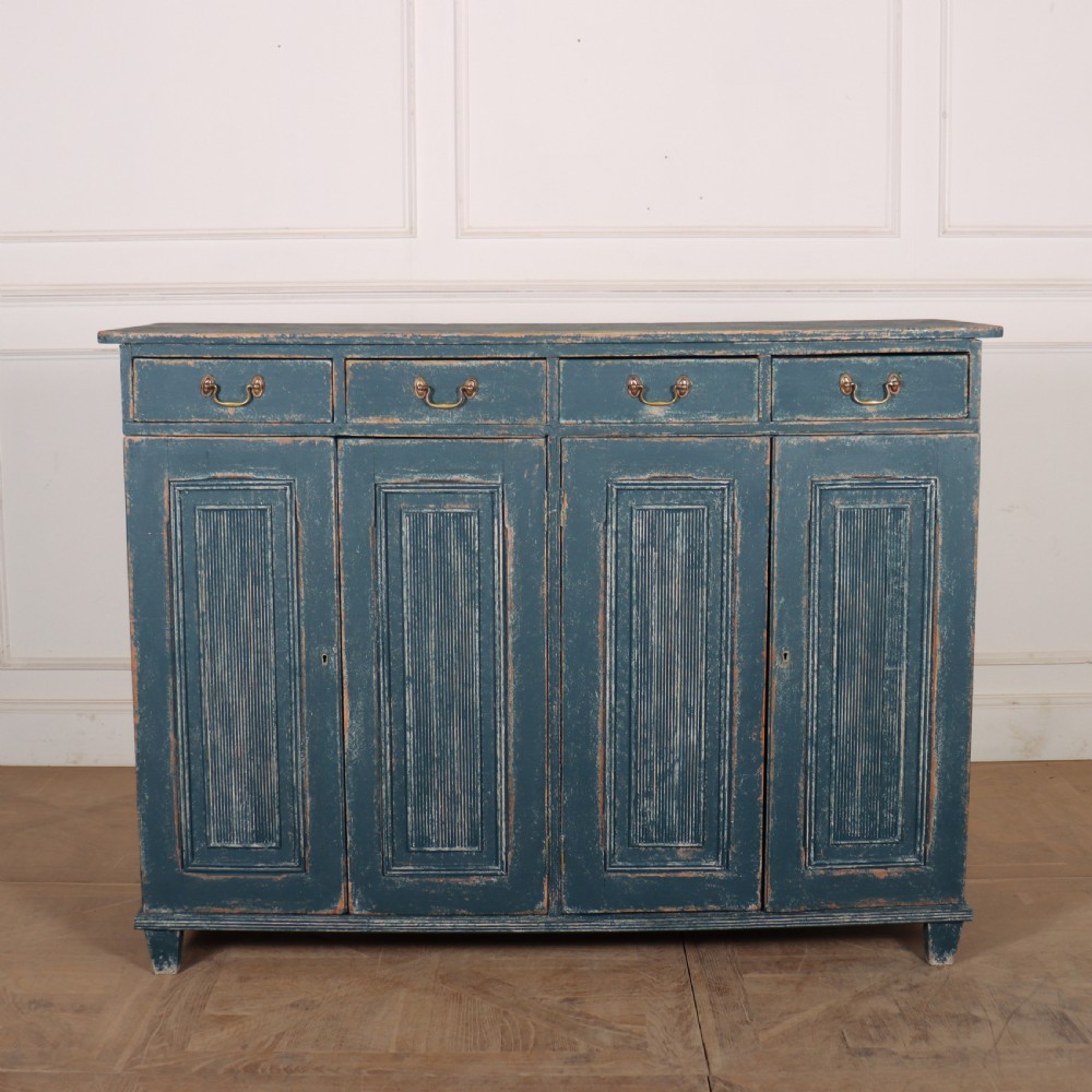 An antique Swedish four-door cupboard featuring a distressed blue painted finish, four top drawers with brass drop handles, and reeded vertical panel doors.