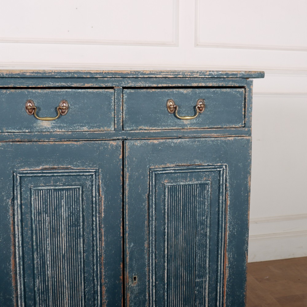 An antique Swedish four-door cupboard featuring a distressed blue painted finish, four top drawers with brass drop handles, and reeded vertical panel doors. View III