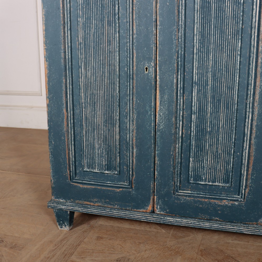An antique Swedish four-door cupboard featuring a distressed blue painted finish, four top drawers with brass drop handles, and reeded vertical panel doors. View IV