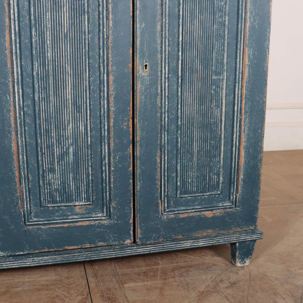An antique Swedish four-door cupboard featuring a distressed blue painted finish, four top drawers with brass drop handles, and reeded vertical panel doors. View V