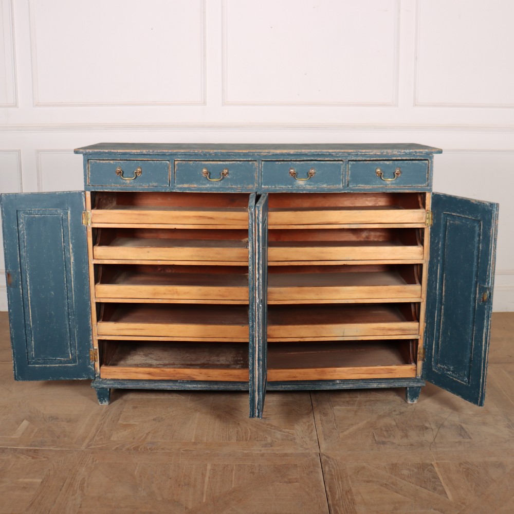 An antique Swedish four-door cupboard featuring a distressed blue painted finish, four top drawers with brass drop handles, and reeded vertical panel doors. View VI