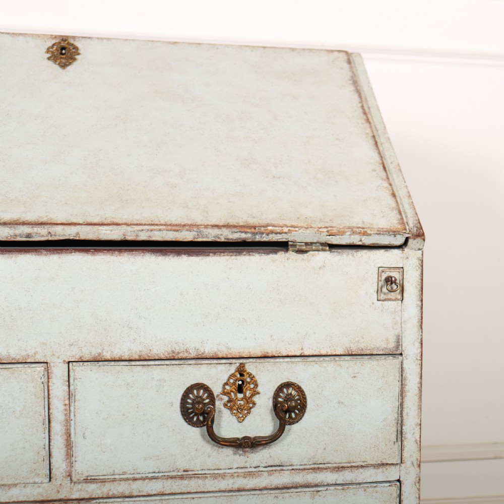 An 18th-century slant-front writing bureau with a distressed off-white painted finish, brass drop handles, and bracket feet. View V