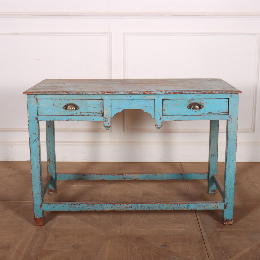 A rectangular wooden table with distressed light blue paint, featuring two drawers with brass cup handles and a low stretcher base.
