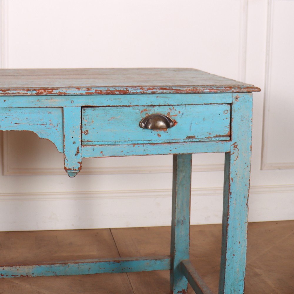 A rectangular wooden table with distressed light blue paint, featuring two drawers with brass cup handles and a low stretcher base. View III