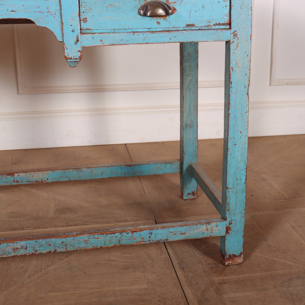 A rectangular wooden table with distressed light blue paint, featuring two drawers with brass cup handles and a low stretcher base. View IV