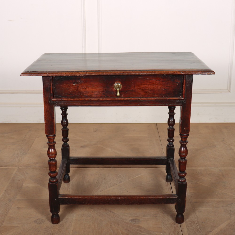 A dark oak 17th-century lamp table featuring a single drawer with a teardrop brass handle, turned baluster legs, and lower box stretchers.
