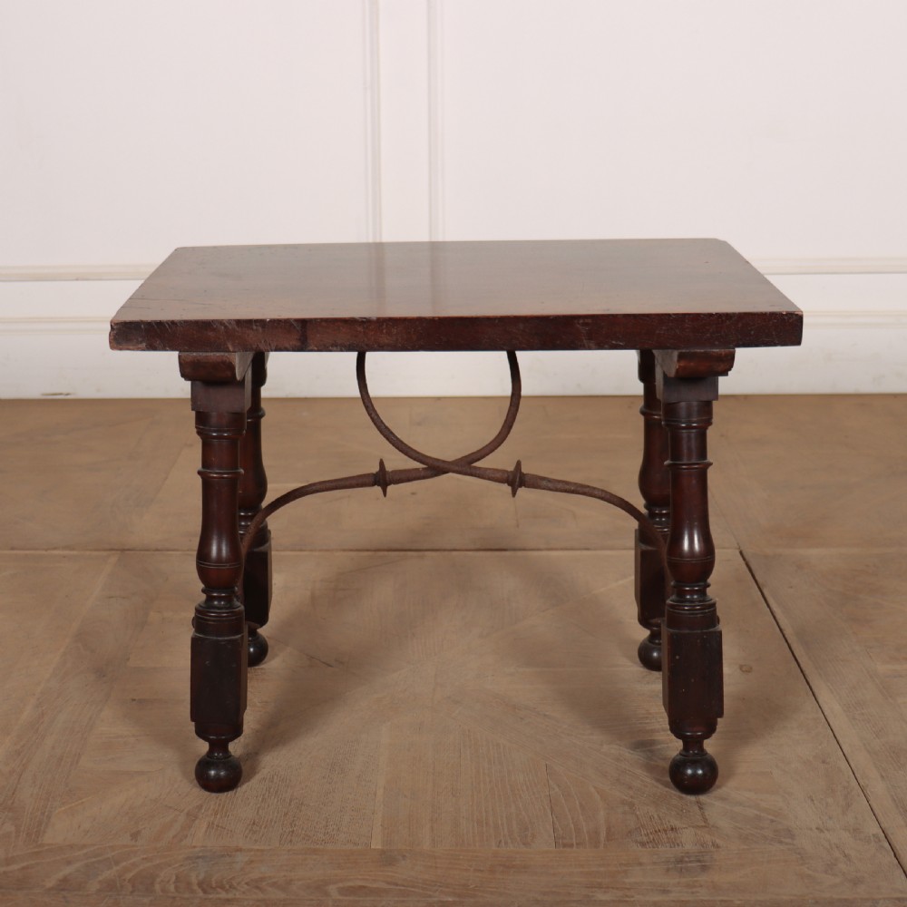 A dark walnut side table featuring turned legs supported by a curved wrought iron stretcher.