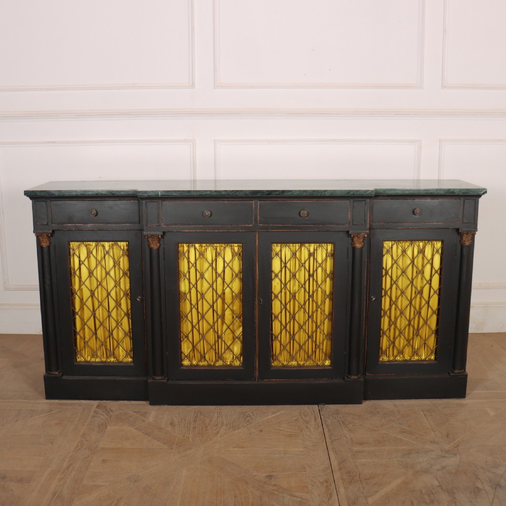 A painted English Regency breakfront dresser base featuring a green marble top, four frieze drawers, Corinthian columns, and mesh doors backed with yellow silk.