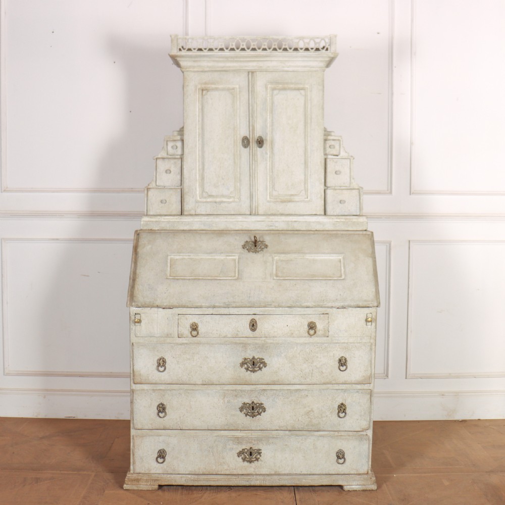 An off-white painted Danish bureau bookcase with a gallery-topped upper cupboard, stepped side drawers, a slant-front desk, and lower drawers fitted with brass lion-head ring handles.
