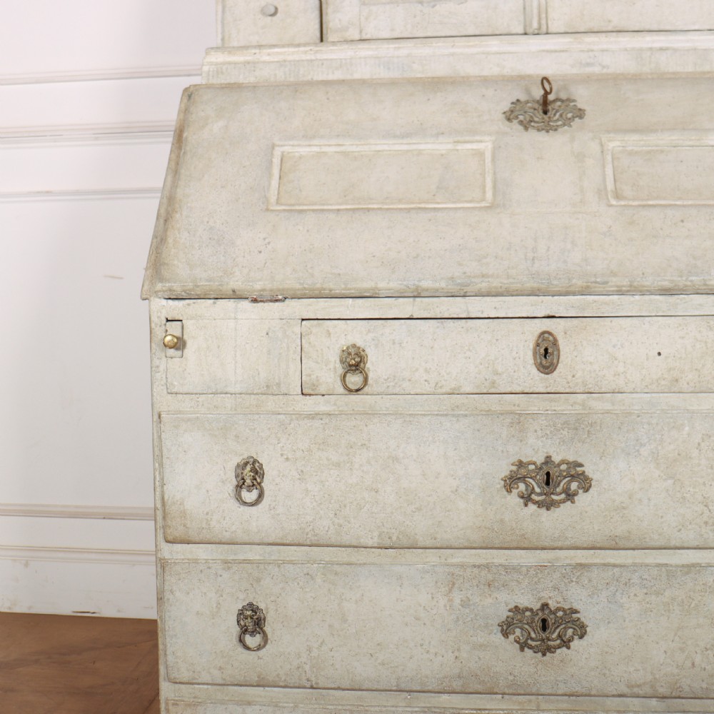 An off-white painted Danish bureau bookcase with a gallery-topped upper cupboard, stepped side drawers, a slant-front desk, and lower drawers fitted with brass lion-head ring handles. View II