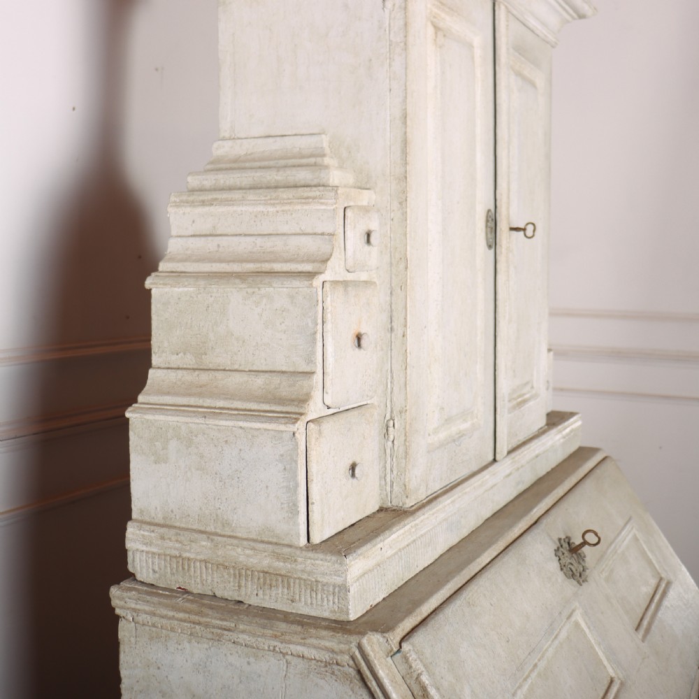 An off-white painted Danish bureau bookcase with a gallery-topped upper cupboard, stepped side drawers, a slant-front desk, and lower drawers fitted with brass lion-head ring handles. View IX