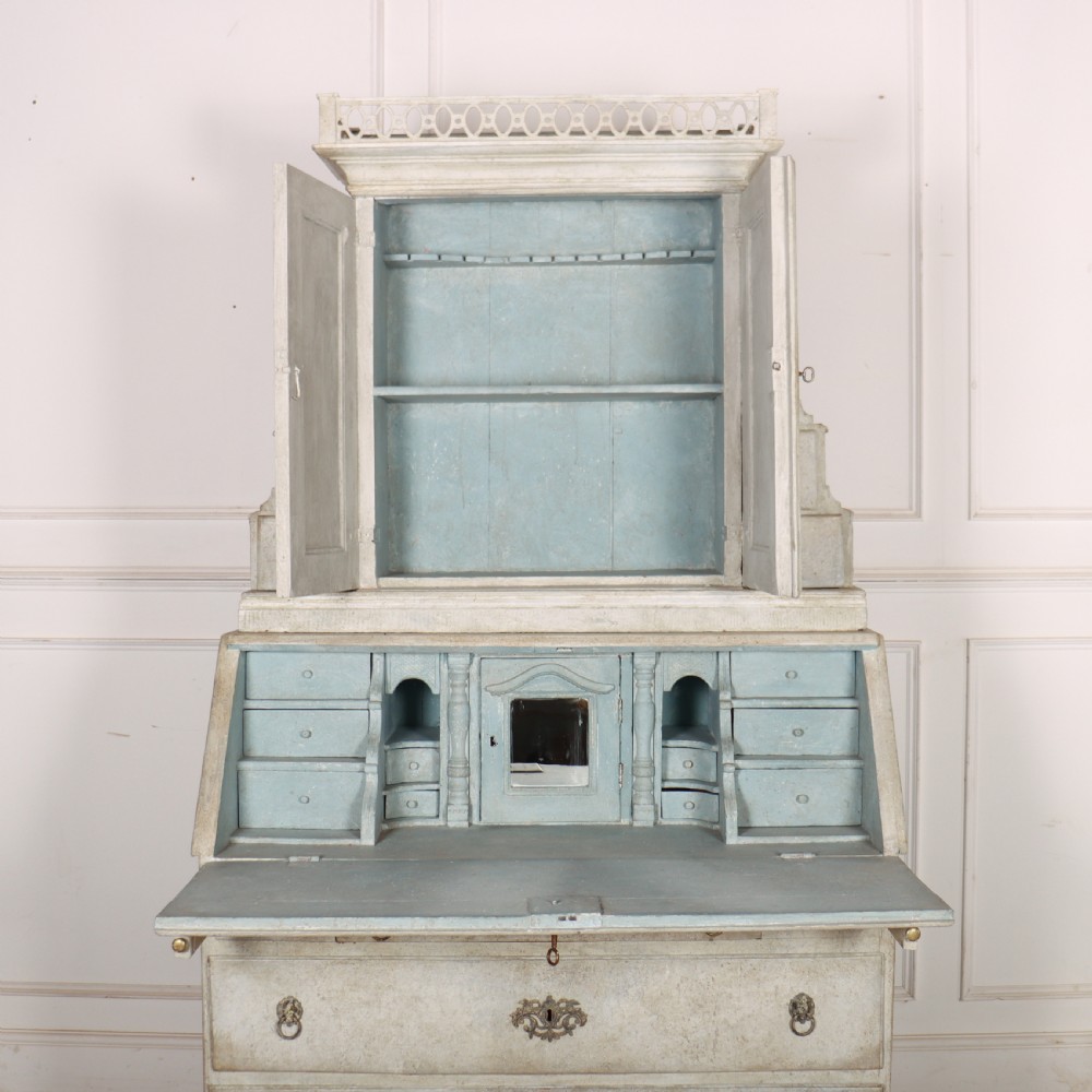 An off-white painted Danish bureau bookcase with a gallery-topped upper cupboard, stepped side drawers, a slant-front desk, and lower drawers fitted with brass lion-head ring handles. View X