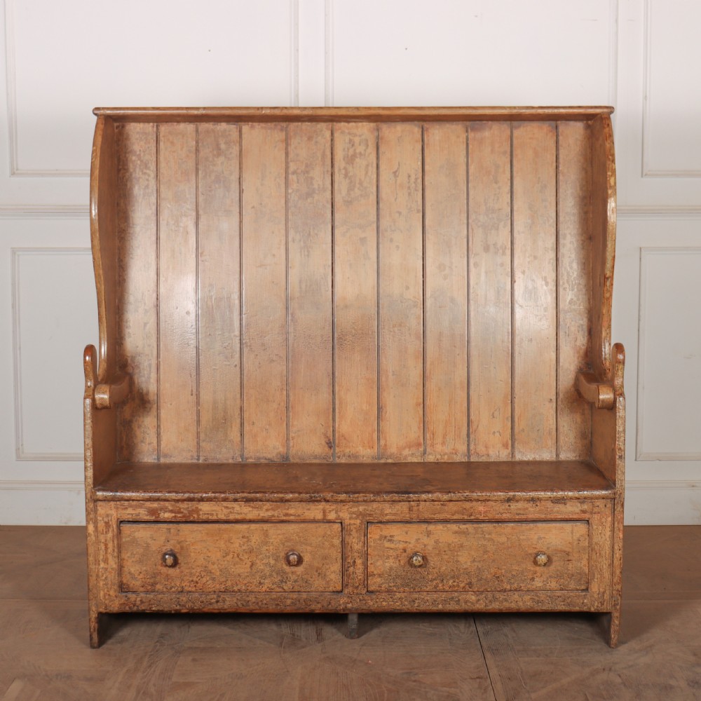 An antique high-backed wooden tavern settle featuring vertical board panelling, shaped side wings, two base drawers, and a distressed painted finish.