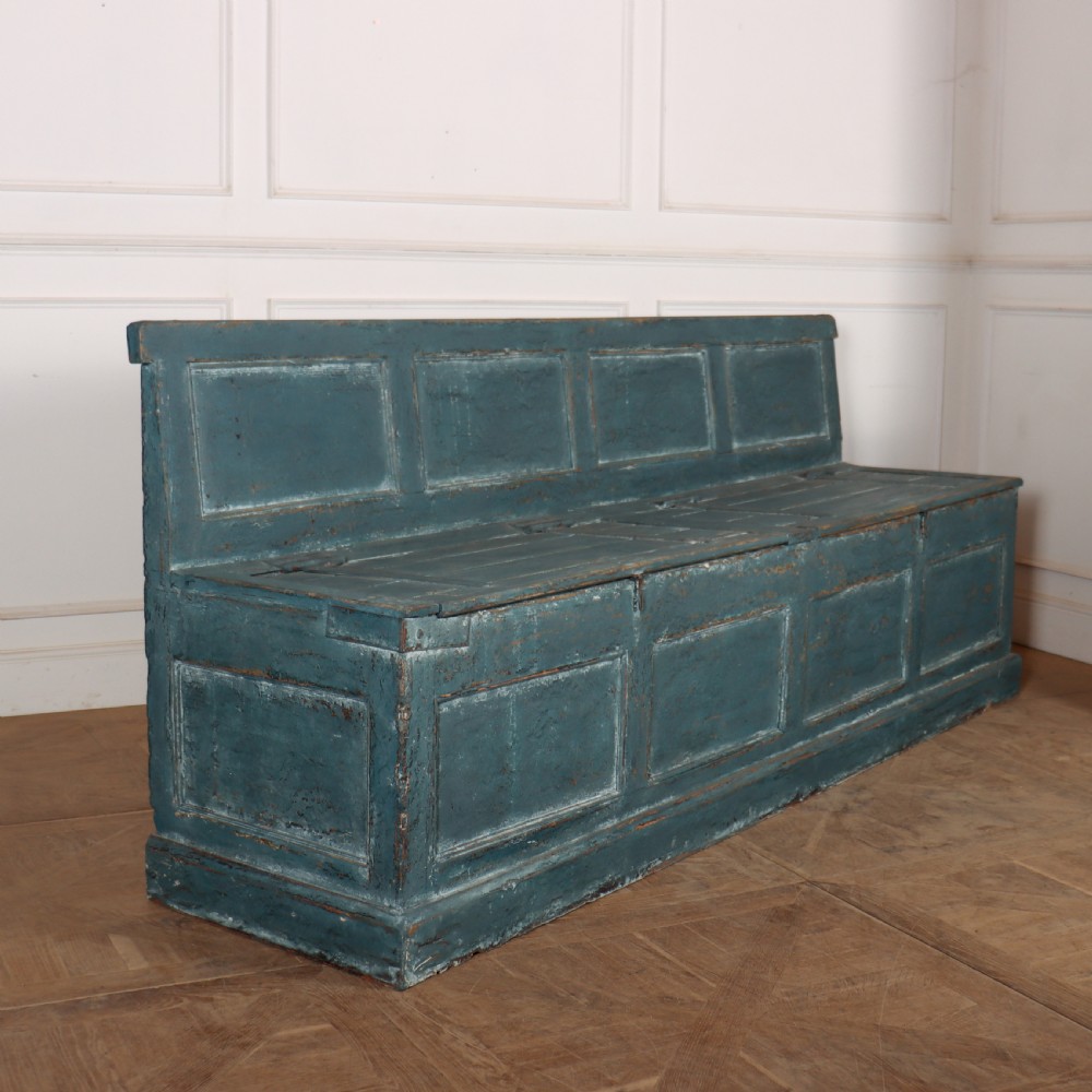A long antique pine settle bench painted in distressed teal blue, featuring a four-panel backrest and a hinged seat lid.