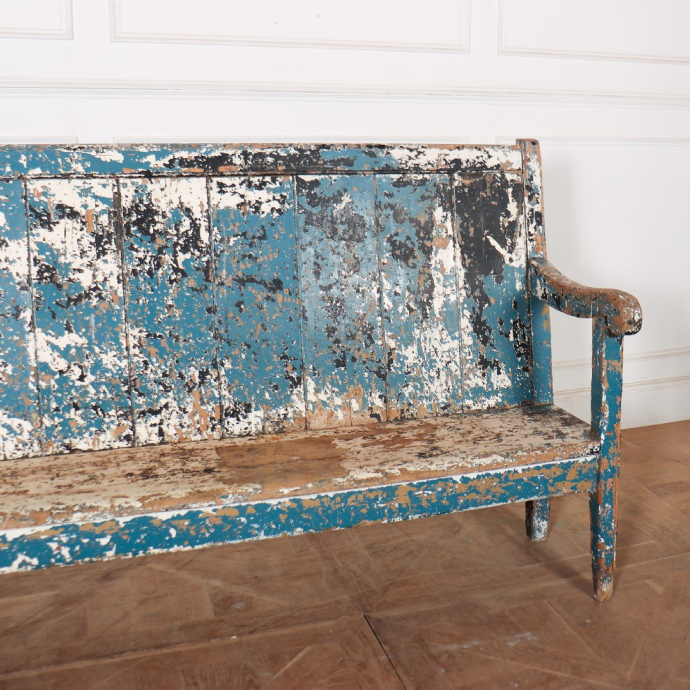 An antique English high back wooden settle bench featuring distressed layers of blue and cream paint with visible exposed timber. View III
