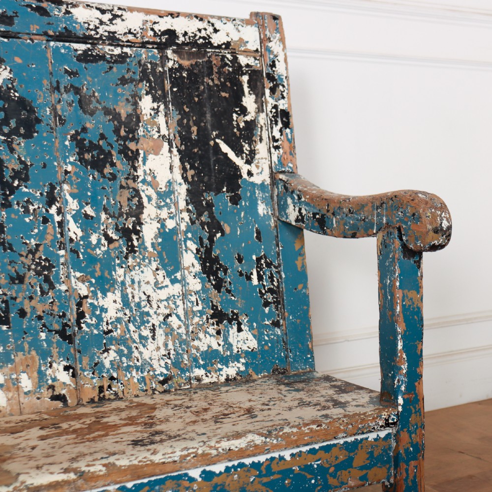 An antique English high back wooden settle bench featuring distressed layers of blue and cream paint with visible exposed timber. View II