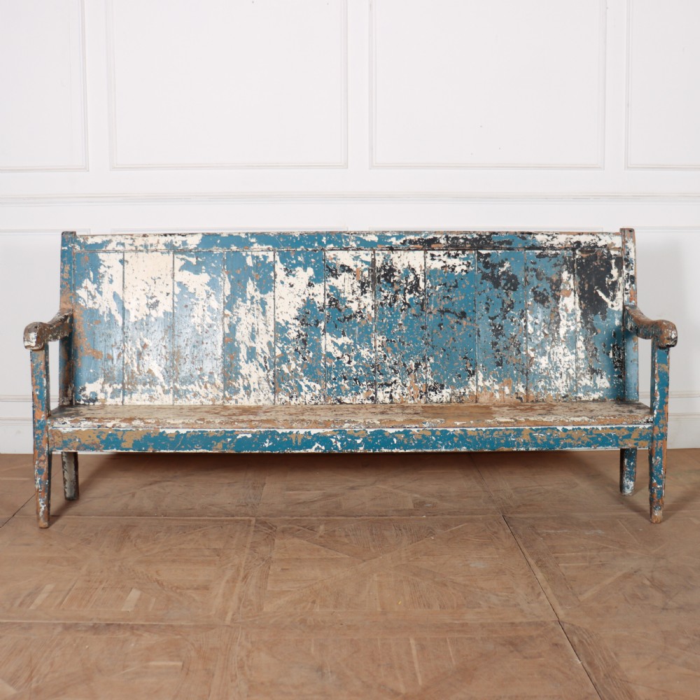 An antique English high back wooden settle bench featuring distressed layers of blue and cream paint with visible exposed timber.