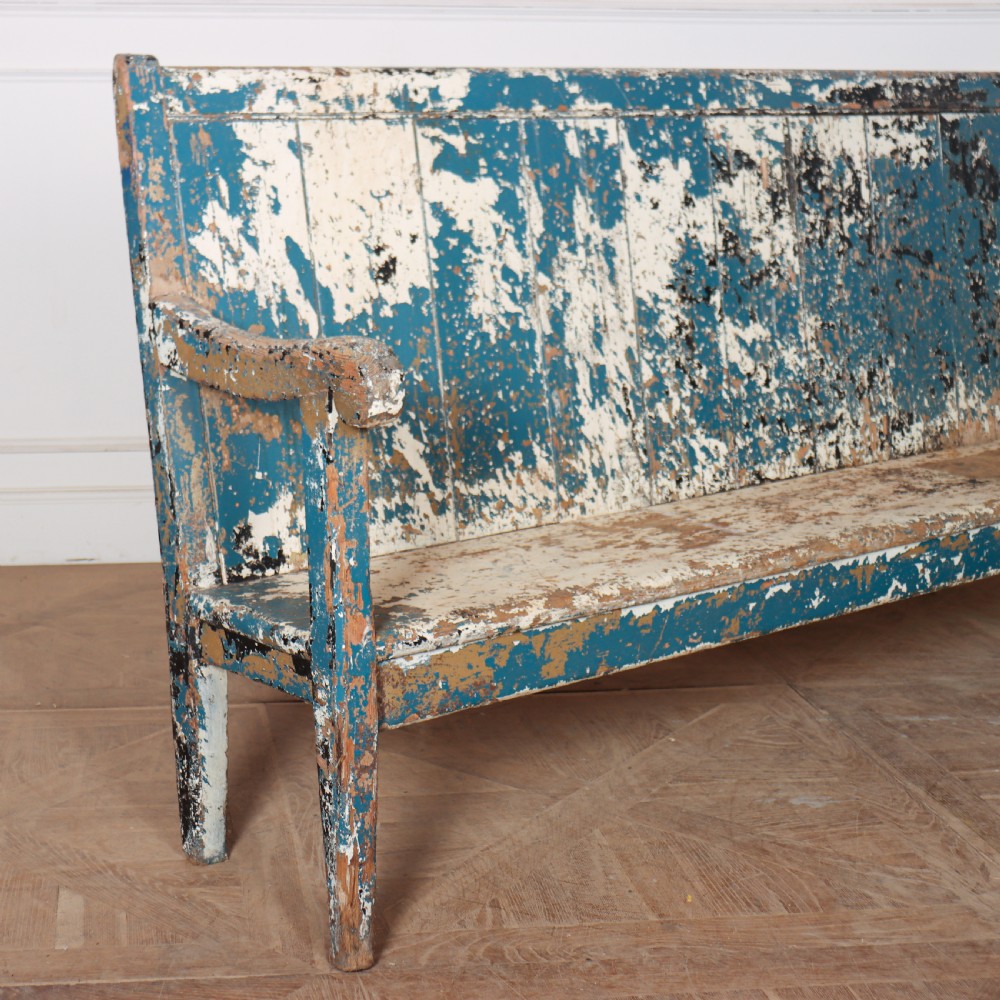An antique English high back wooden settle bench featuring distressed layers of blue and cream paint with visible exposed timber. View VI