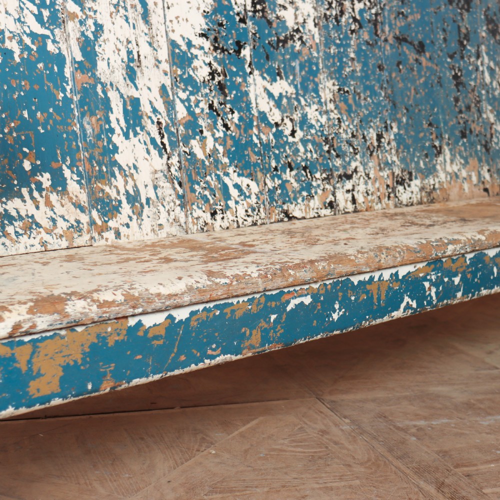 An antique English high back wooden settle bench featuring distressed layers of blue and cream paint with visible exposed timber. View IX