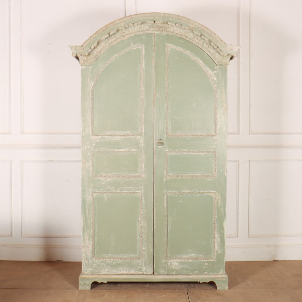 A 19th-century green painted wooden wardrobe featuring an arched carved cresting, double panelled doors, and a distressed finish.