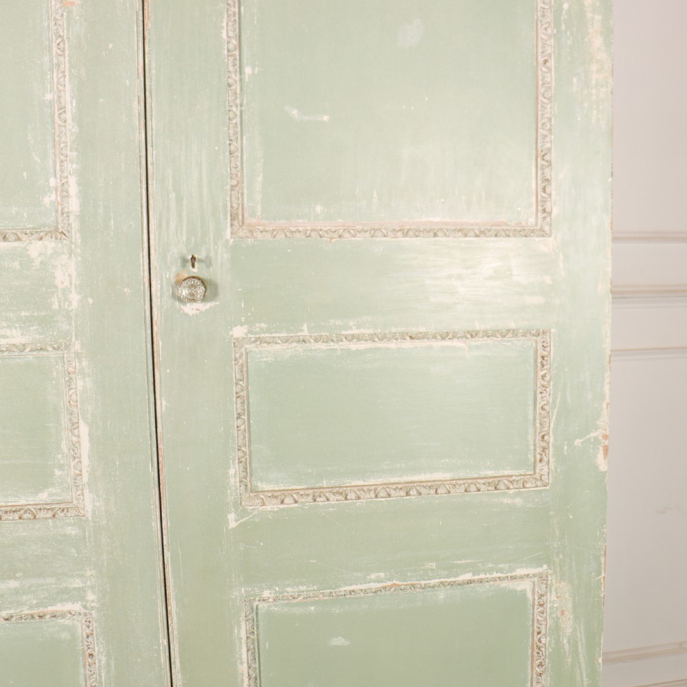 A 19th-century green painted wooden wardrobe featuring an arched carved cresting, double panelled doors, and a distressed finish. View V