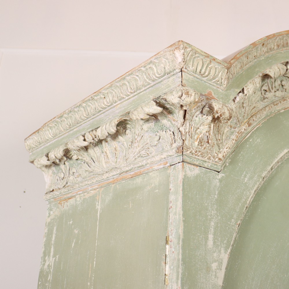 A 19th-century green painted wooden wardrobe featuring an arched carved cresting, double panelled doors, and a distressed finish. View X