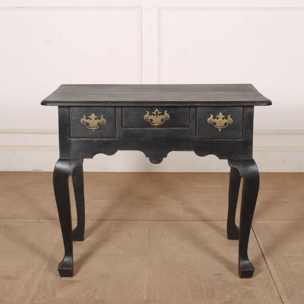 A black painted antique lowboy table featuring three drawers with brass batwing handles, a shaped apron, and cabriole legs.