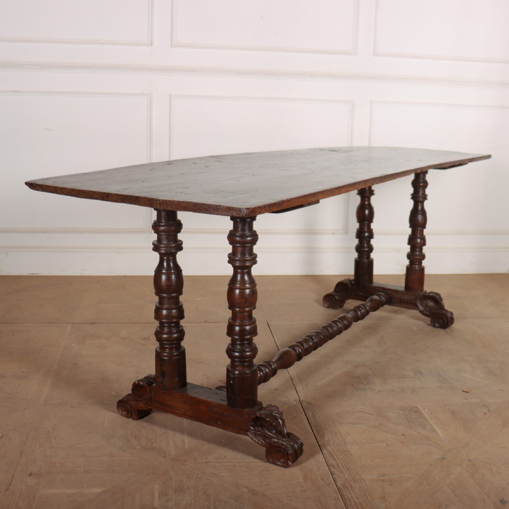 An antique dark walnut trestle table featuring turned baluster legs, carved scroll feet, and a turned central stretcher.