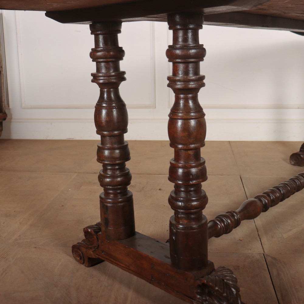 An antique dark walnut trestle table featuring turned baluster legs, carved scroll feet, and a turned central stretcher. View III