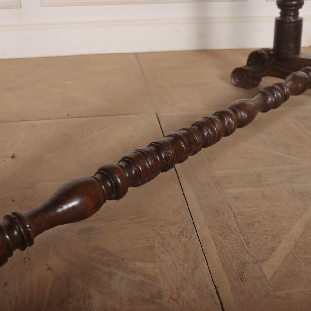 An antique dark walnut trestle table featuring turned baluster legs, carved scroll feet, and a turned central stretcher. View IV