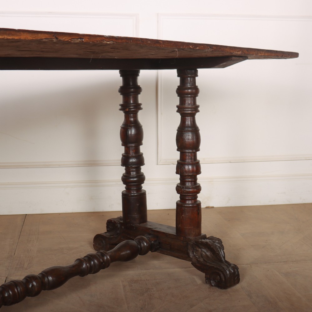 An antique dark walnut trestle table featuring turned baluster legs, carved scroll feet, and a turned central stretcher. View V
