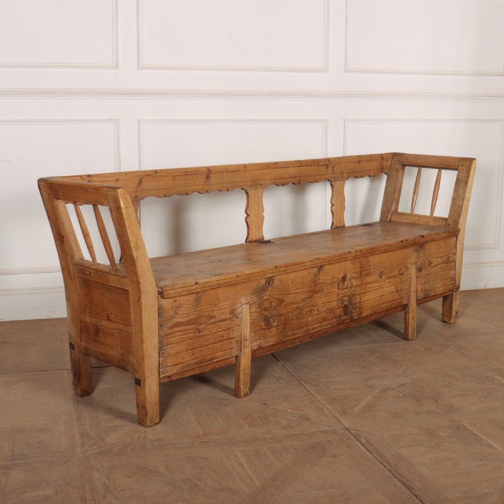 A nineteenth-century Swedish pine settle bench featuring open spindled side panels, a scalloped backrail, and a lift-top storage seat base.