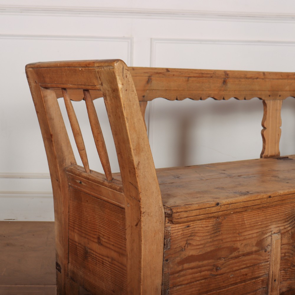 A nineteenth-century Swedish pine settle bench featuring open spindled side panels, a scalloped backrail, and a lift-top storage seat base. View II