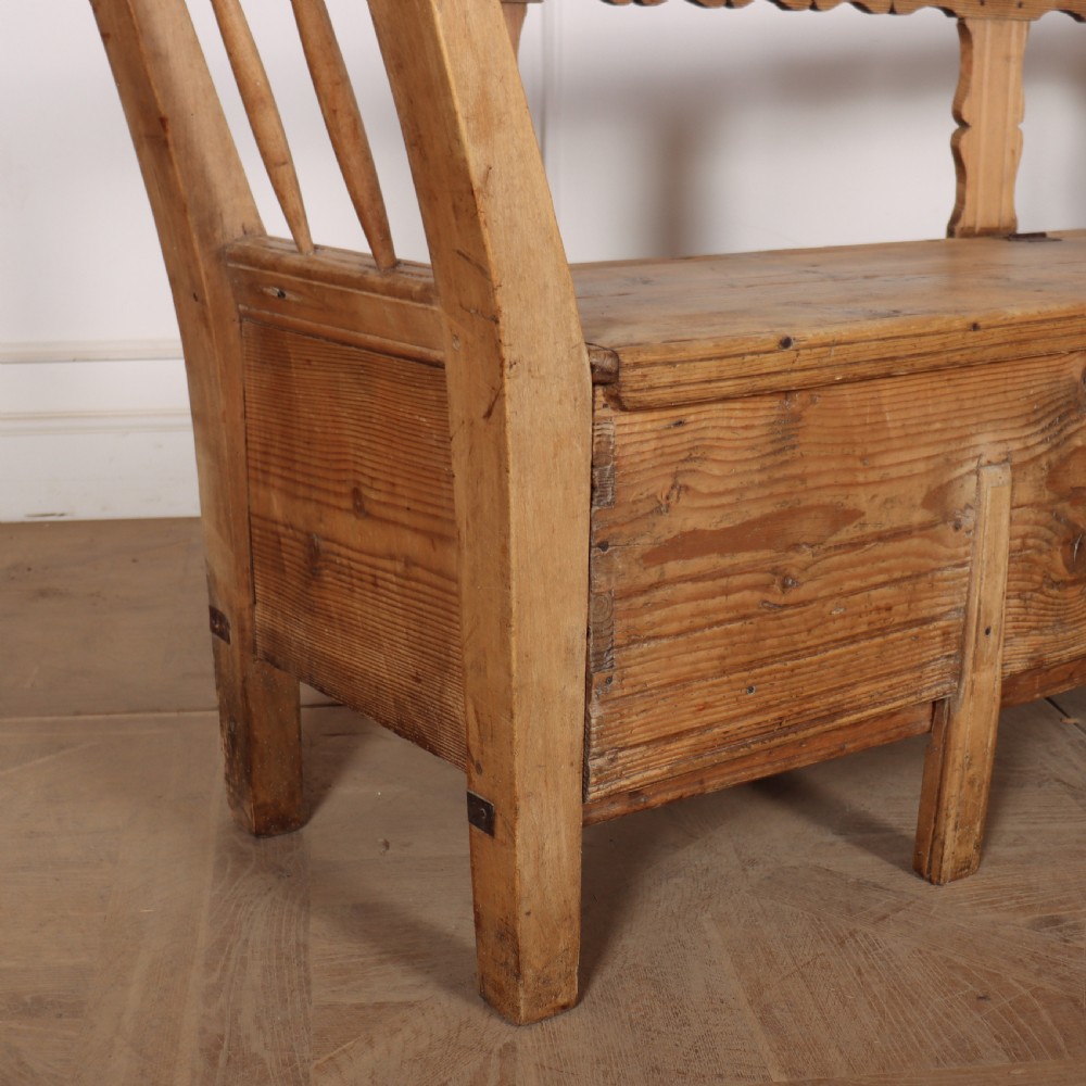 A nineteenth-century Swedish pine settle bench featuring open spindled side panels, a scalloped backrail, and a lift-top storage seat base. View III