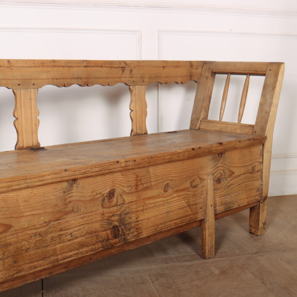 A nineteenth-century Swedish pine settle bench featuring open spindled side panels, a scalloped backrail, and a lift-top storage seat base. View IV