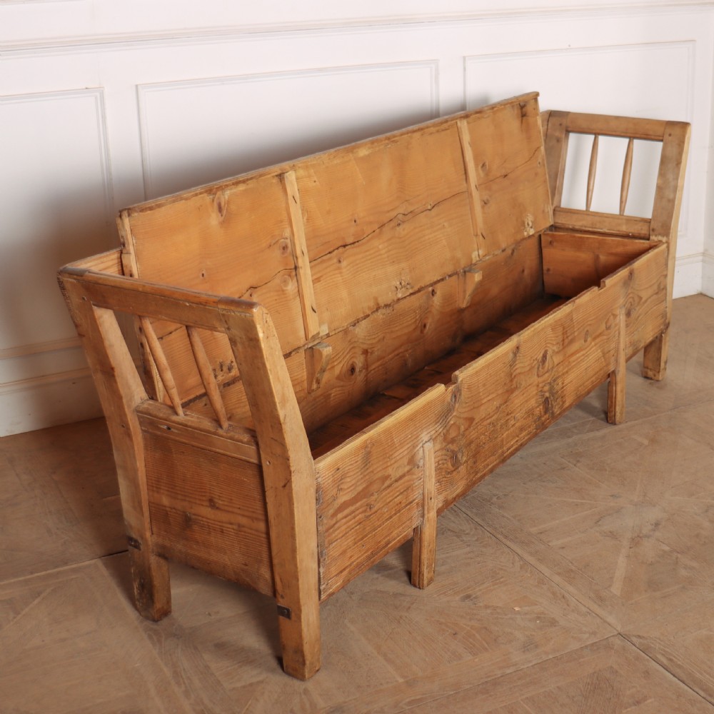 A nineteenth-century Swedish pine settle bench featuring open spindled side panels, a scalloped backrail, and a lift-top storage seat base. View V