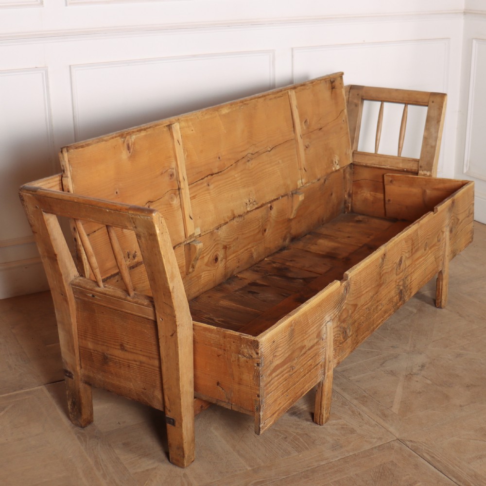 A nineteenth-century Swedish pine settle bench featuring open spindled side panels, a scalloped backrail, and a lift-top storage seat base. View VII