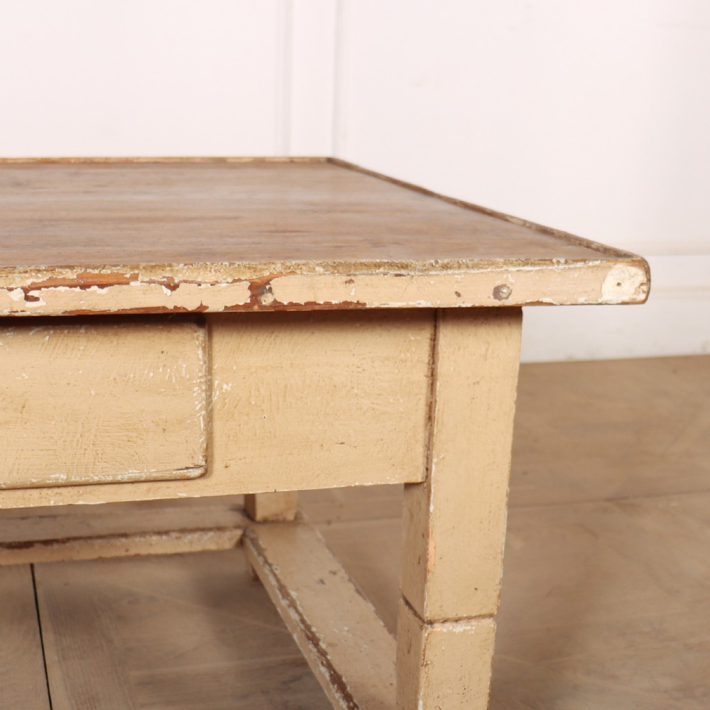A rectangular low painted coffee table featuring a distressed cream paint finish, a single drawer with a metal drop handle, and a perimeter floor stretcher. View V