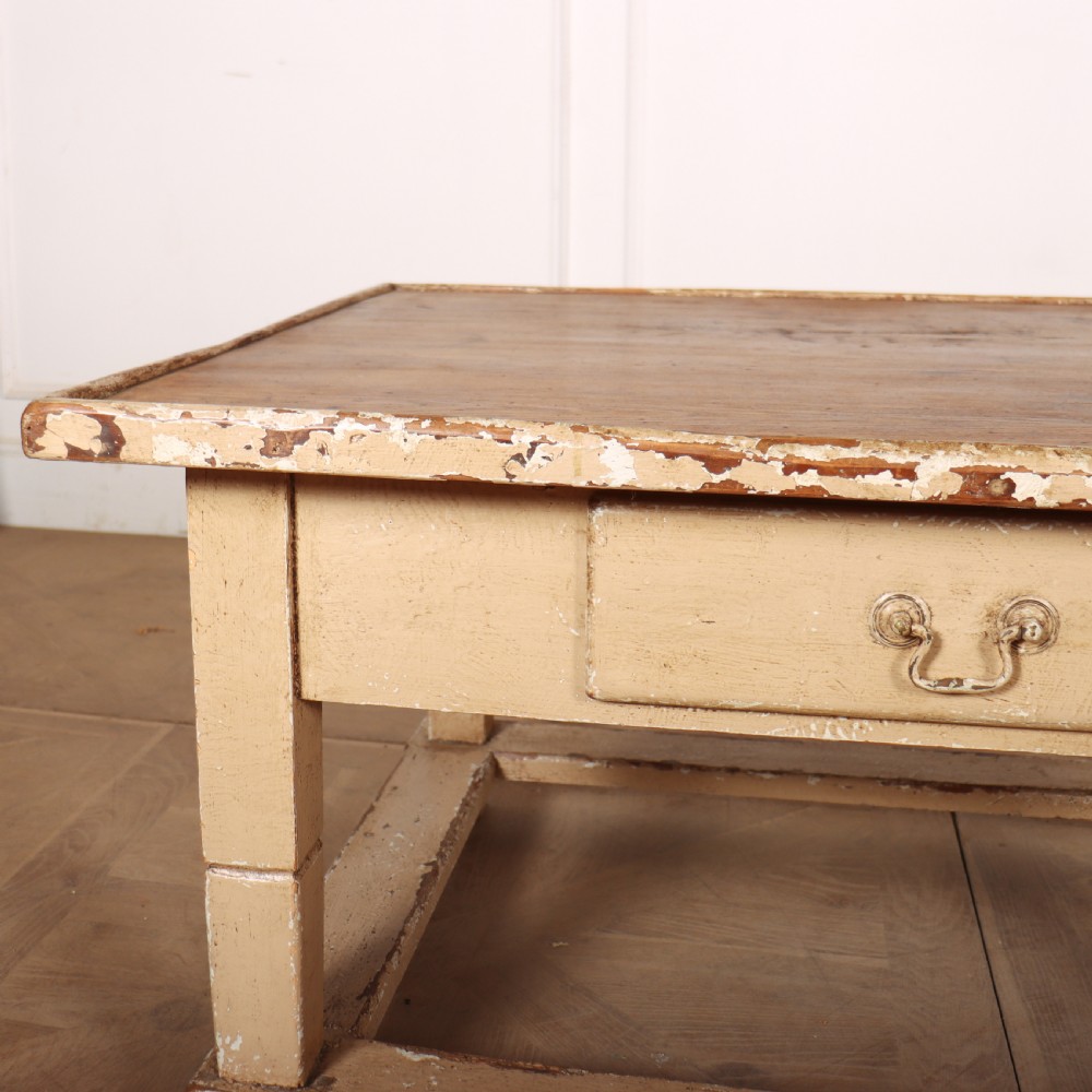 A rectangular low painted coffee table featuring a distressed cream paint finish, a single drawer with a metal drop handle, and a perimeter floor stretcher. View VI