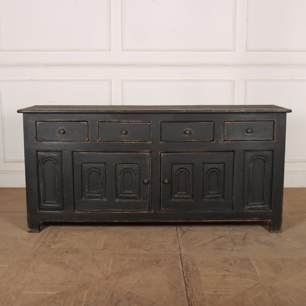 An 18th-century dark painted wooden dresser base featuring four frieze drawers above recessed cupboard doors decorated with geometric arch mouldings.