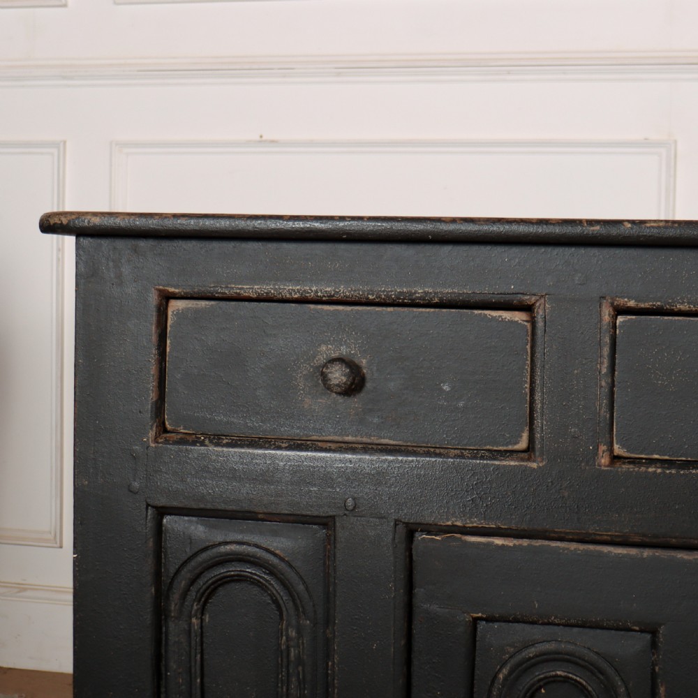 An 18th-century dark painted wooden dresser base featuring four frieze drawers above recessed cupboard doors decorated with geometric arch mouldings. View II