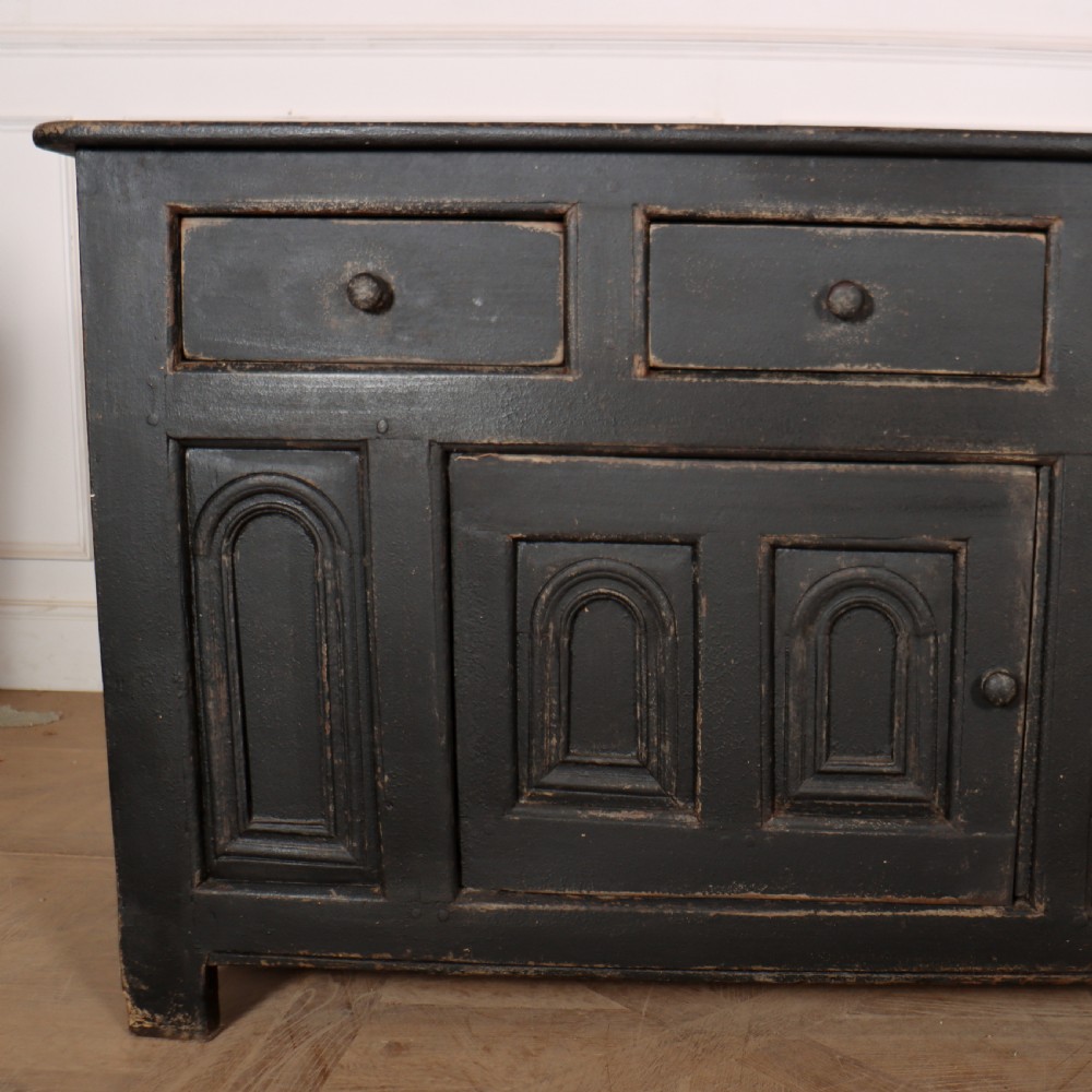 An 18th-century dark painted wooden dresser base featuring four frieze drawers above recessed cupboard doors decorated with geometric arch mouldings. View IV