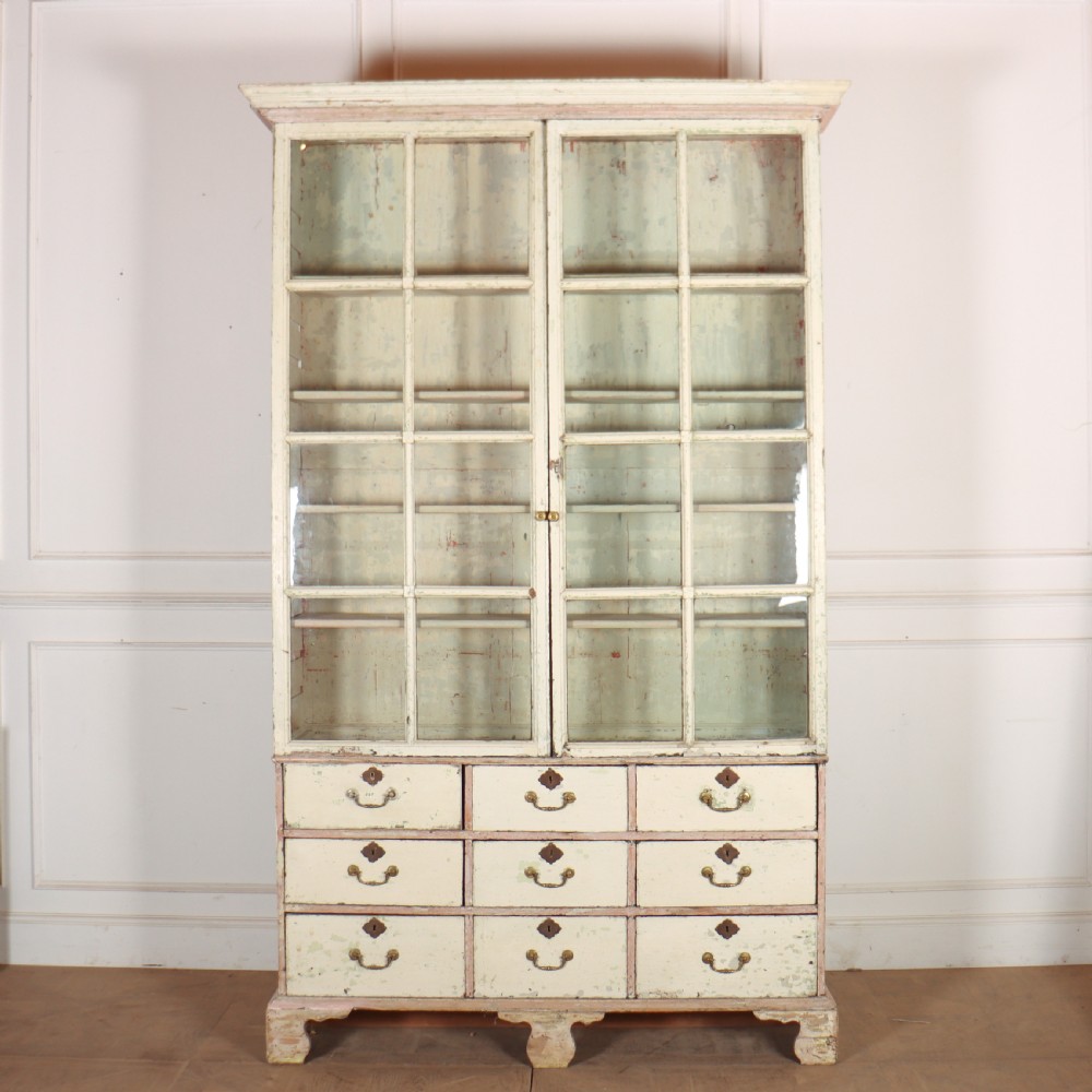 A tall Georgian painted bookcase featuring two multi-pane glazed doors above nine drawers with brass handles.