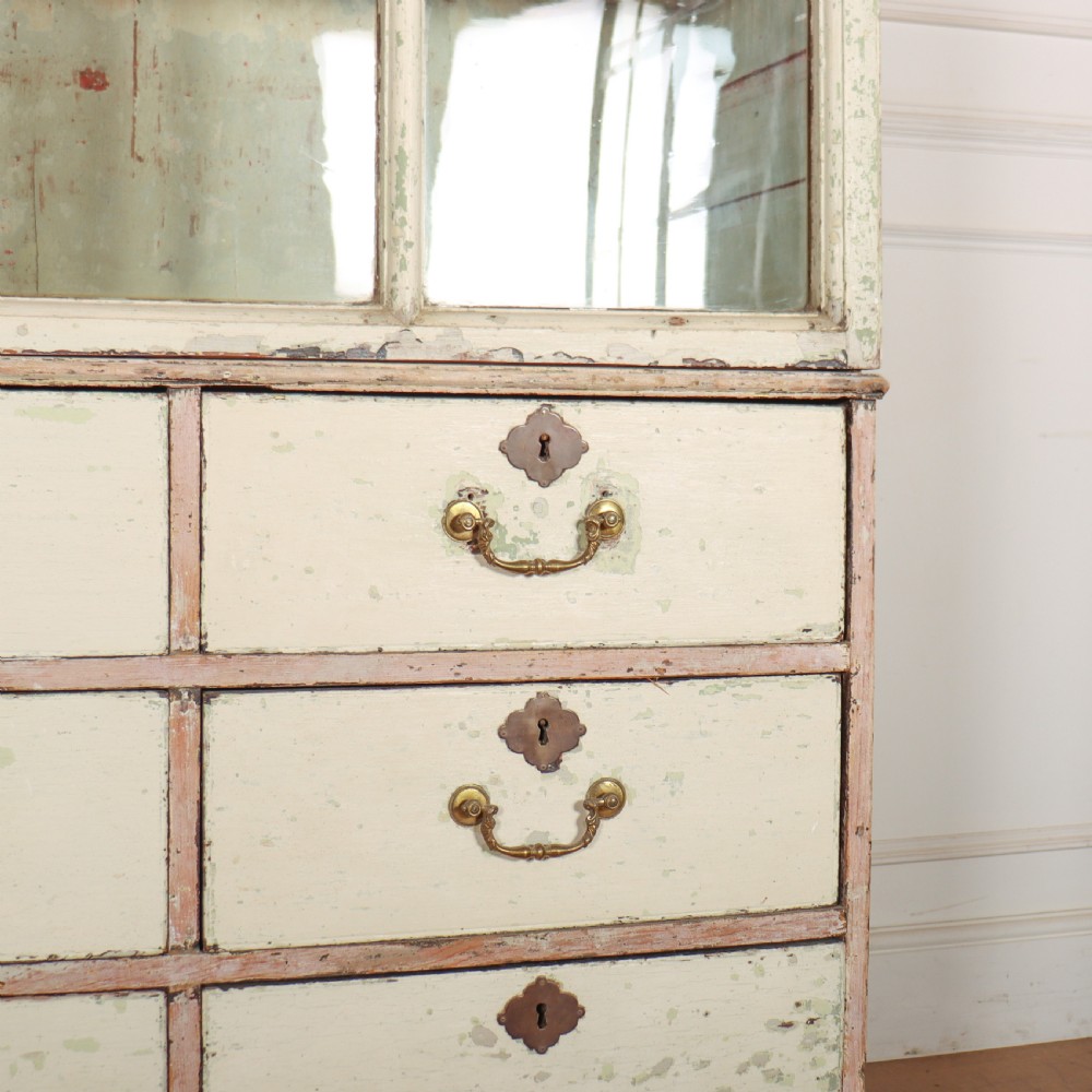 A tall Georgian painted bookcase featuring two multi-pane glazed doors above nine drawers with brass handles. View VII